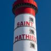 Ein vertikaler LilleEiland - Kalender 2025 für September mit dem Phare de Saint-Mathieu, einem hohen, schlanken Leuchtturm auf einer Klippe. Der Leuchtturm ist weiß mit roten Details und blickt auf eine Grasfläche
