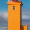 Eine lebendige Werbung mit dem hohen, gelben Leuchtturm von Stafnes vor einem klaren Himmel, darüber ein LilleEiland - Kalender 2025 für November und eine Karte, die seine Lage im Nordatlantik hervorhebt