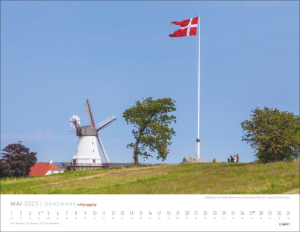 Kalenderbild für DÄNEMARK - richtig hyggelig 2025 mit einer dänischen Landschaft mit einem großen Fahnenmast, an dem die dänische Flagge weht, und einer altmodischen Windmühle auf einem sanften Hügel. Ein klarer blauer Himmel und ein paar Menschen