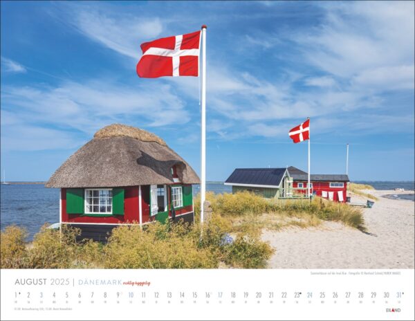 Eine DÄNEMARK – richtig hyggelig-Kalenderseite 2025 für August, die eine hyggelig-schöne Strandszene in Dänemark mit zwei traditionellen dänischen Häusern mit Strohdächern unter wehenden dänischen Flaggen, einem klaren blauen Himmel darüber und einer ruhigen See zeigt.