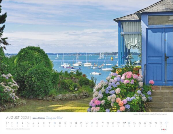 Ein „Mein kleines Haus am Meer“-Kalender für 2025 mit einer ruhigen Meeresaussicht neben einer blauen Holzhütte, übersät mit üppigen rosa Hortensien und einem klaren Blick auf ankernde Segelboote in der Ferne.