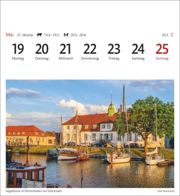 Eine Kalenderseite, die eine Woche im Mai mit den Daten 19–25 zeigt, beschriftet auf Deutsch. Jeder Tag von Montag bis Sonntag hat ein Kästchen, wobei der 25. hervorgehoben ist. Das Bild unten zeigt Segelboote in einem ruhigen Yachthafen in Glückstadt bei Sonnenuntergang.