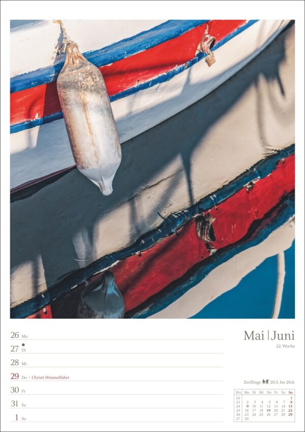 Eine Nahaufnahme eines frisch gefangenen Fisches, der an der Seite eines farbenfroh blau und rot bemalten Bootes hängt, mit sichtbaren Texturen der abgenutzten Bootsoberfläche und den glänzenden Schuppen des Fisches. Das Bild ist vor einem klaren blauen Himmel zu sehen.