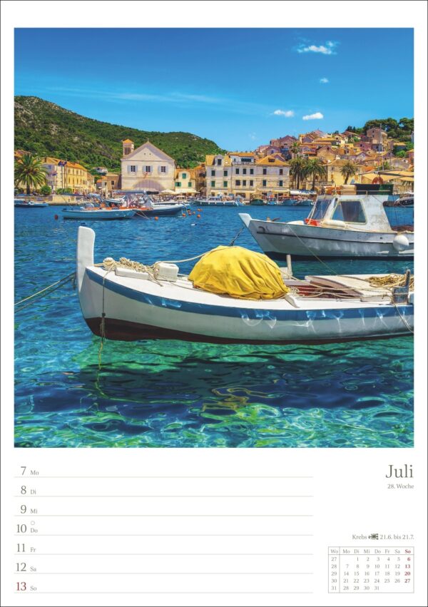 Ein lebendiges Kalenderbild für Juli, das ein malerisches mediterranes Dorf mit historischen Steingebäuden neben ruhigem, azurblauem Wasser zeigt. Im Vordergrund liegt ein Holzboot mit gelber Abdeckung vor Anker, darüber ein klarer Himmel.