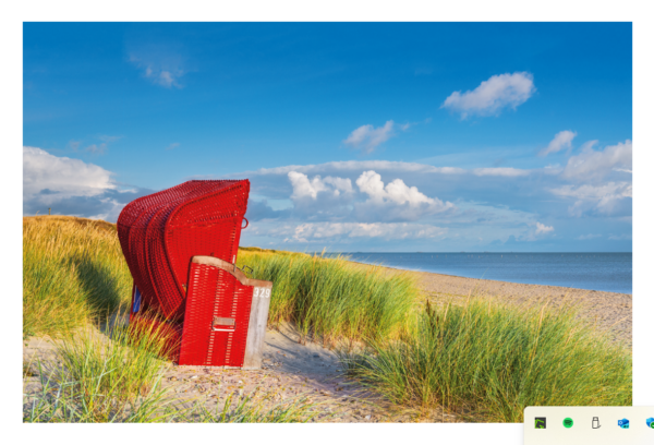Ein roter Strandkorb aus Korbgeflecht mit der Nummer 729, eingebettet zwischen grünem Dünengras unter einem strahlend blauen Himmel mit flauschigen Wolken, mit Blick auf einen sandigen Küstenlandstrand und das ruhige Meer.