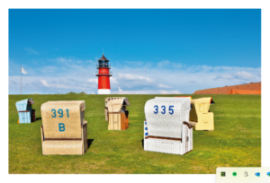 Drei bunte Strandstühle mit den Nummern 391b, 335 und einem weiteren ohne Nummer stehen auf leuchtend grünem Gras unter einem klaren blauen Himmel in Beach Chairland. Im Hintergrund ein