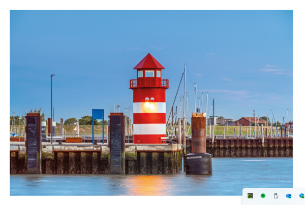 Ein leuchtend roter Leuchtturm mit spitzem Dach und weißen Fenstern steht am Eingang eines Yachthafens auf FÖHR ...meine Insel, wo mehrere Segelboote unter einem klaren blauen Himmel vor Anker liegen.