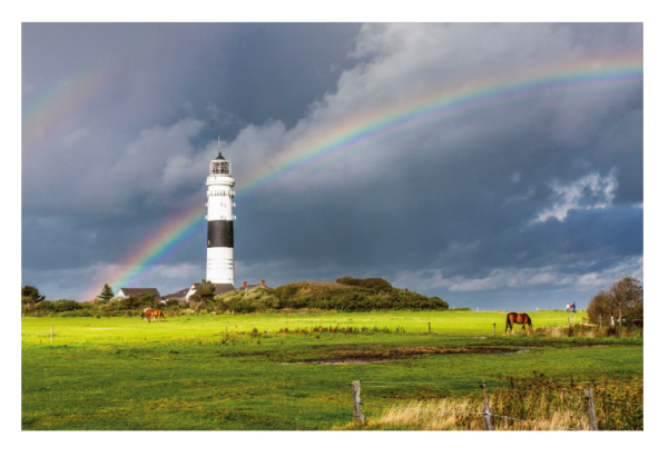 Ein Leuchtturm steht auf einem grasbewachsenen Hügel im Küstenland Esszimmer unter einem stürmischen Himmel, über dem sich ein heller doppelter Regenbogen wölbt. Zwei Pferde grasen im Vordergrund des üppigen Grüns
