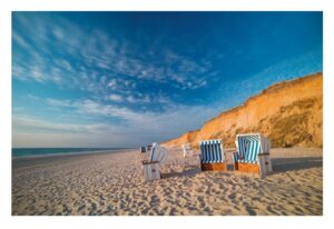 Drei Strandstühle von Sylt ...meine Insel stehen auf der Insel Sylt mit Blick auf das Meer, vor der Kulisse einer Sandklippe unter einem blauen Himmel mit dünnen Wolken. Die Szene fängt eine ruhige Strandumgebung an einem sonnigen Tag ein.