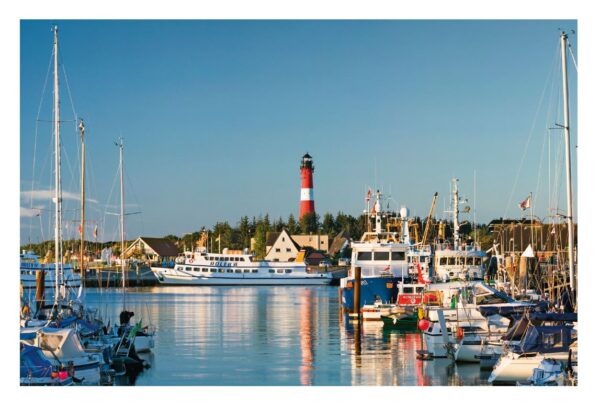 Eine malerische Hafenszene auf der Insel SYLT ...meine Insel mit einer Vielzahl von Booten, darunter Segelboote und Fischerboote, die im ruhigen blauen Wasser vor Anker liegen. Ein Leuchtturm mit roten und weißen Streifen steht